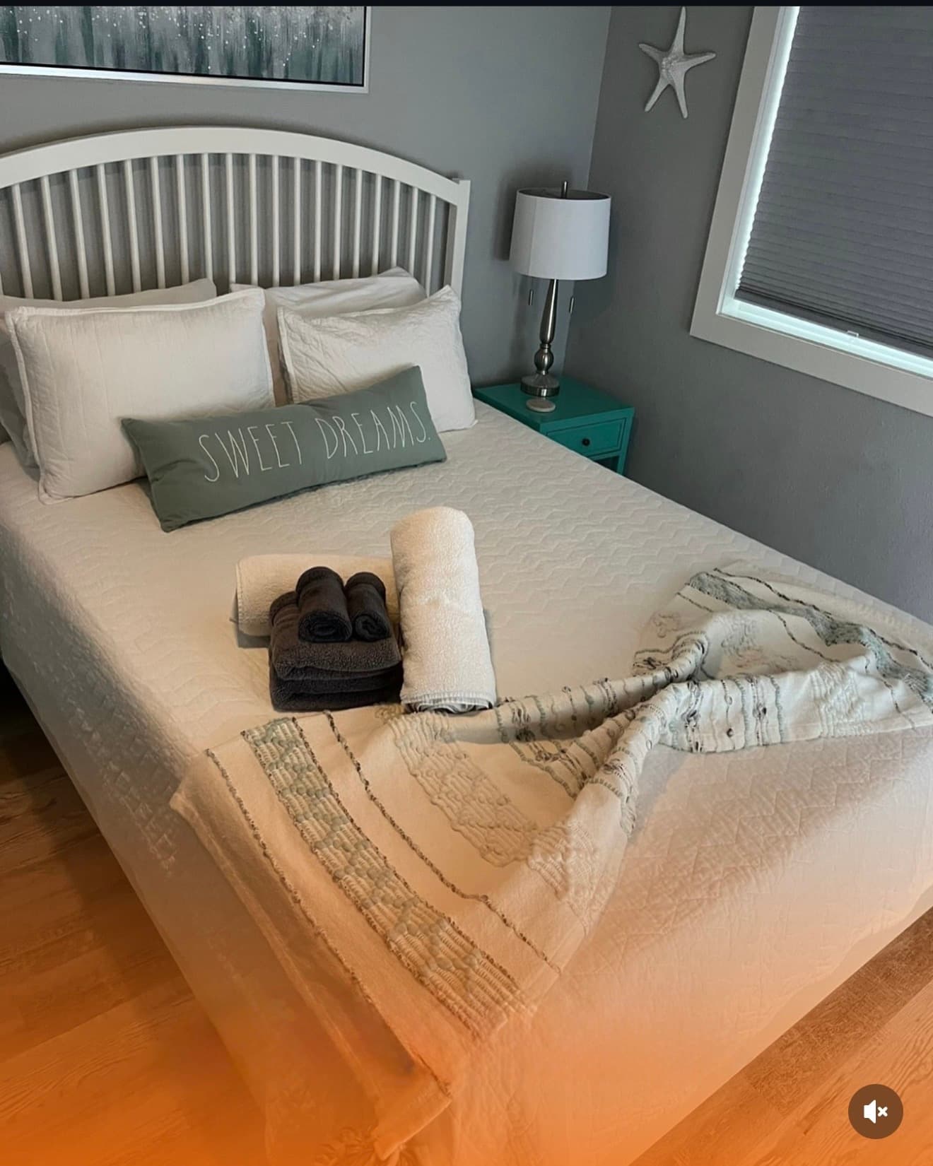 White bed with a green 'Sweet Dreams' pillow, folded towels, and a teal nightstand.