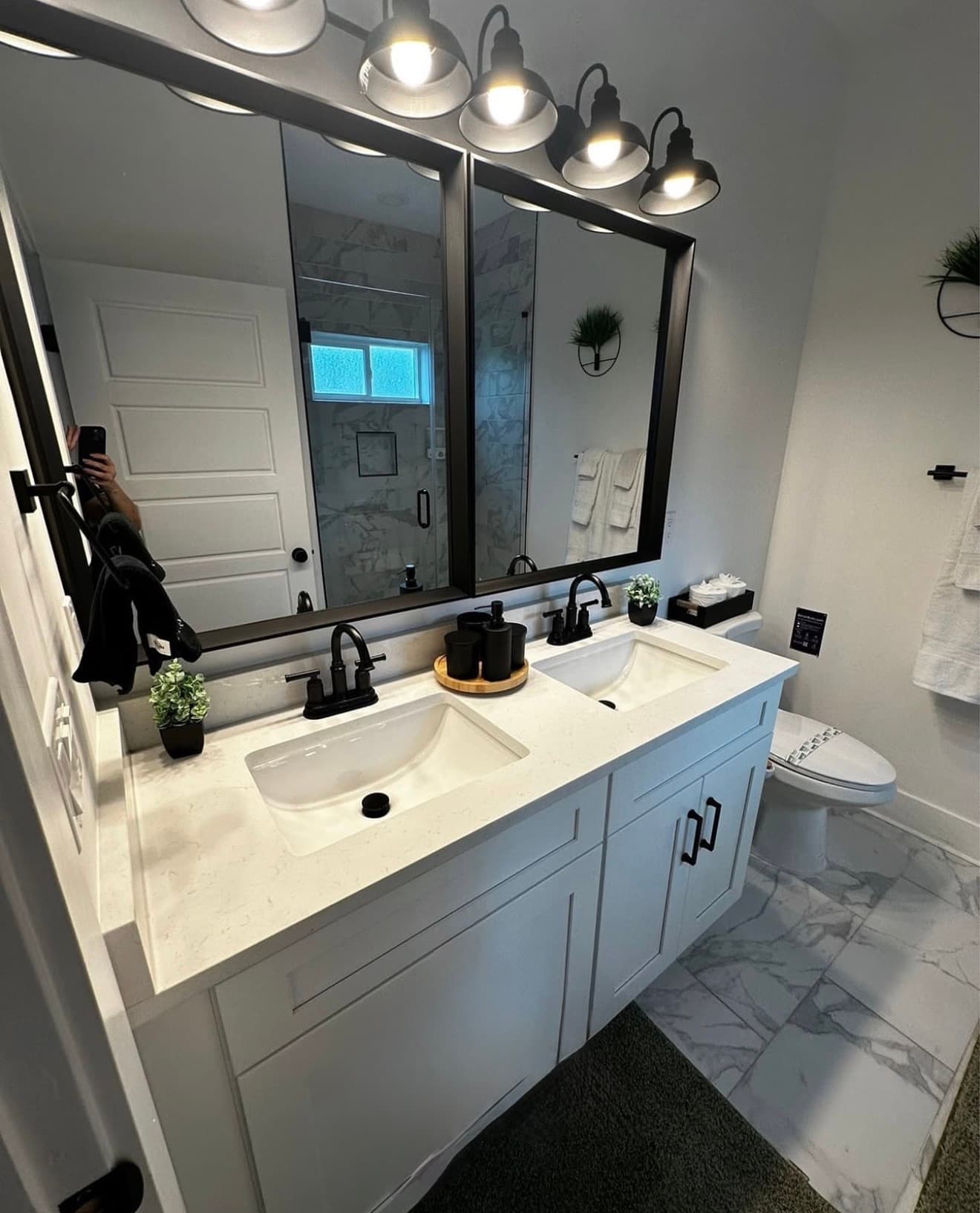 Modern bathroom with white double vanity, black fixtures, large mirror, and marble tile flooring.